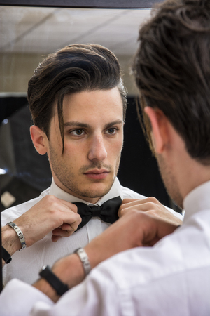 Mirror reflection of elegant handsome man wearing bow-tie and looking at himselfの写真素材
