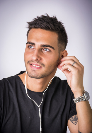 Attractive young man with earphones listening to music, on light backgroundの写真素材