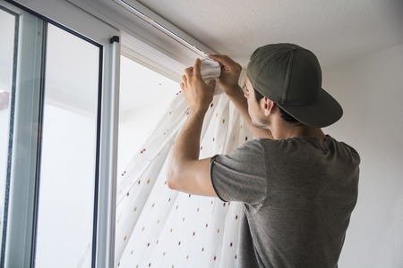 Young handsome man or handyman installing curtains over window at home, doing renovation workの写真素材