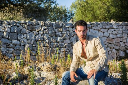 Ruggedly Handsome Man Among Trees with Shirt Unbuttoned Relaxing in Warm Sunlightの写真素材