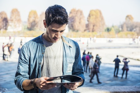 Half Body Shot of a Thoughtful Handsome Young Man, a Tourist, Holding a Guide, Looking Away Outside Historic Building in European Cityの写真素材