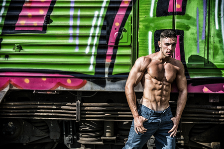 Portrait of young shirtless man with sexy body posing against of old train while looking downの写真素材