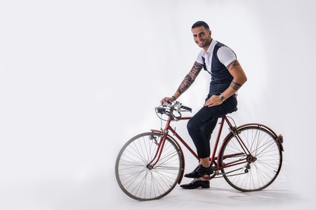 Portrait of young tattooed man in elegant clothes and shoes riding a bicycle.Isolate.Studio shot.の写真素材