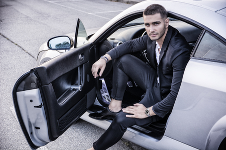 Portrait of young attractiave man in business suit sitting in his new stylish polished car outdoorの写真素材