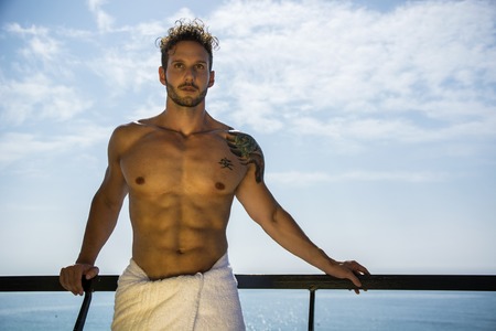 Muscular young man leaning on metal hand-railing on cruise ship, looking at cameraの写真素材