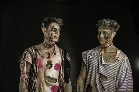 Two male zombies standing on black background, looking at each other smilingの写真素材