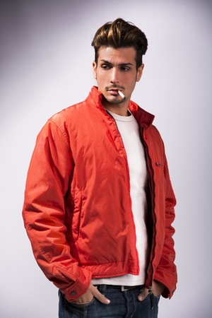Handsome young man smoking cigarette, dressed as James Dean with red jacket on light backgroundの写真素材