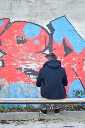Young man seen from the back looking at a graffiti covered wallの写真素材