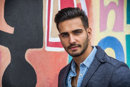 Attractive young man standing against colorful graffiti wall, looking at cameraの写真素材