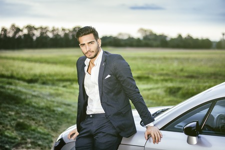 Portrait of young attractiave man in business suit sitting in his new stylish car outdoor in countrysideの写真素材