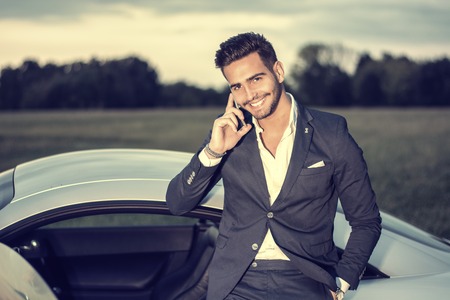 Portrait of young attractiave man in business suit sitting in his new stylish car outdoor in countrysideの写真素材
