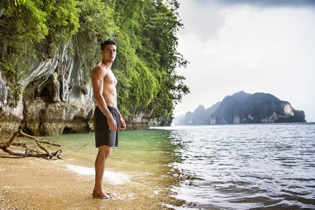 Full length shot of a young man standing on a beach in Phi Phi Island, Thailand, shirtless wearing boxer shorts, showing muscular fit bodyの写真素材