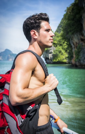 Portrait of young handsome bare chested brunet man?looking away against seascape on a boat or ship, leaning on handrailの写真素材