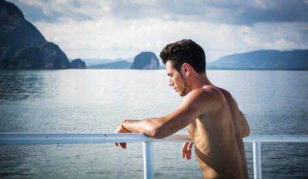 Portrait of young handsome bare chested brunet man?looking away against seascape on a boat or ship, leaning on handrailの写真素材