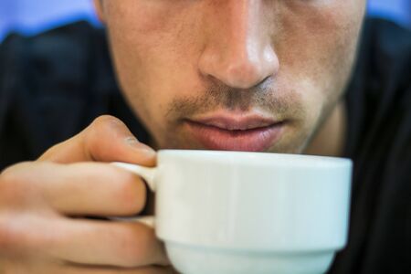 Close-up of young man drinking coffee or tea from white cupの写真素材