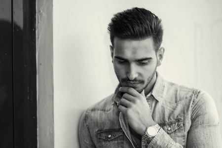 Attractive young man sitting against colorful wall, looking away to a sideの写真素材