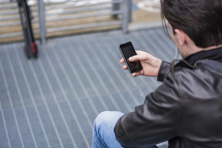 Handsome young man standing outdoors in urban environment on metal stairs, using cell phoneの写真素材