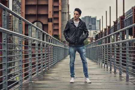 Handsome young man standing outdoors in urban environment on metal stairs, looking at cameraの写真素材