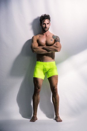 Handsome shirtless muscular man in briefs, standing, on light background in studio shotの写真素材