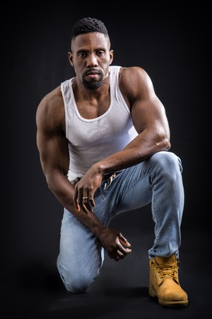 Male black bodybuilder wearing white tanktop on ripped muscular torso in studio shot on black backgroundの写真素材