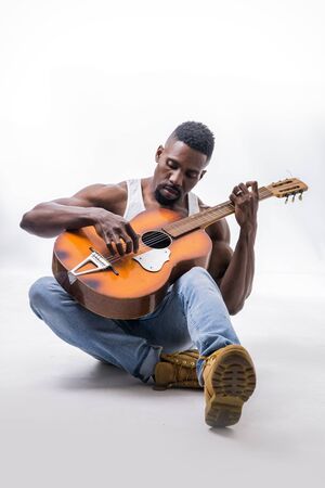 Muscular black man playing guitar, wearing jeans and white tank-topの写真素材