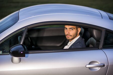Portrait of young attractiave man in business suit sitting in his new stylish car outdoor in countrysideの写真素材