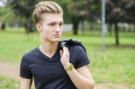 Attractive blond young man outdoors in a park, smilingの写真素材