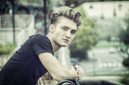 Profile shot of attractive blond young man in city, looking at camera, outdoorの写真素材