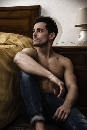 Handsome young man sitting next to his bed with serious expression, staring in the void with a blank lookの写真素材