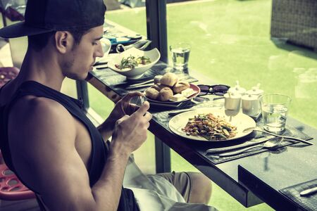 Side view of a handsome young man taking a photo of his food in the restaurant. Horizontal indoors...