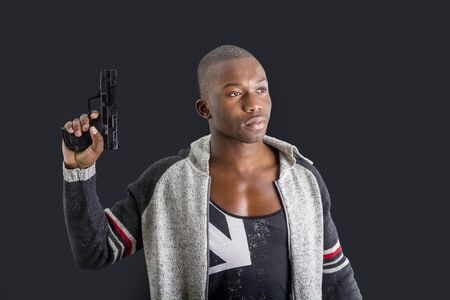 Young handsome black man holding a hand gun, on dark background in studioの写真素材
