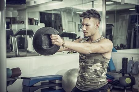 Attractive young athletic man exercising in gym, working out using kettlebell