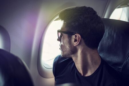 Side view of handsome young man against plane window sitting and looking outの写真素材