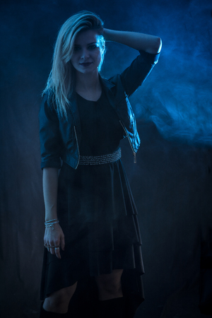 Portrait of attractive blonde woman in black skirt and leather jacket looking at camera in studio shot, on dark backgroundの写真素材