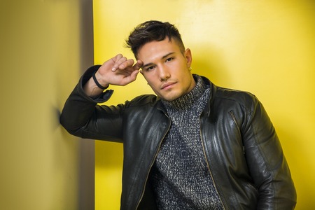 Handsome white asian young man wearing black leather jacket standing on yellow background against...