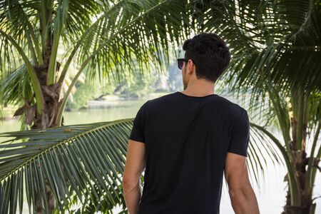 Back of young man outdoor in nature, near palm trees in a sunny day