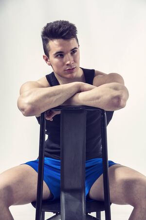 Handsome young muscular man sitting on chair in studio shot over neutral backgroundの写真素材