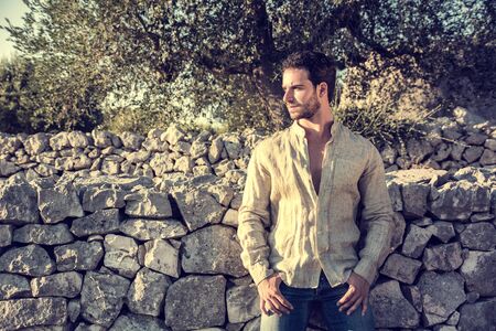 Ruggedly Handsome Man Among Trees with Shirt Unbuttoned Relaxing in Warm Sunlightの写真素材