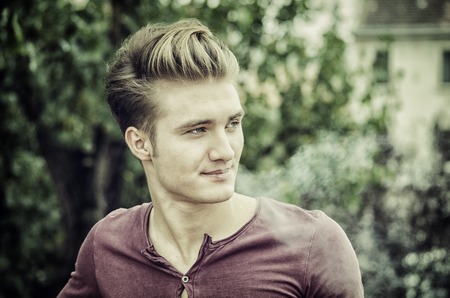 Handsome blond young man outdoors smoking cigarette, looking away to a sideの写真素材