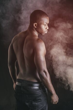 Handsome shirtless muscular black young man, looking at camera, on dark background in studio shotの写真素材