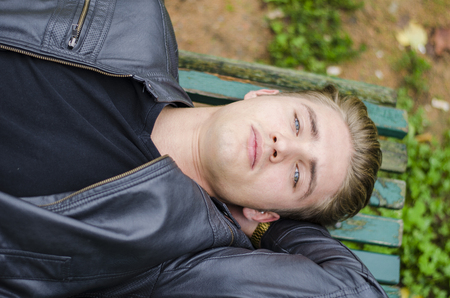 Handsome blond young man laying on green, wooden park bench. thinkingの写真素材