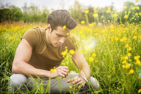 Attractive, fit young man relaxing sitting on lawn in the countryside among grass, looking away, smilingの写真素材
