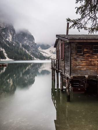 View to beautiful calm lake in forest in mountains, with a wooden hut, cabana or small house on the waterの写真素材