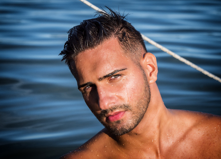 Attractive young shirtless athletic man standing in water in sea or lake, wearing shorts, looking at cameraの写真素材