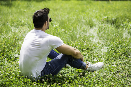 Handsome Muscular Hunk Man Outdoor in City Park or Countryside, Sitting on Grass. Showing Healthy Muscle Body While Looking awayの写真素材