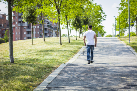 Back of muscular man in city park in a nice summer day walking. Full length shotの写真素材