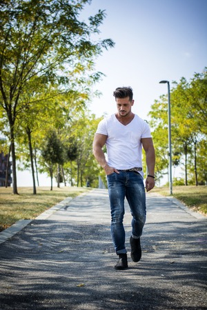 Attractive muscular man in city park in a nice summer day walking. Full length shotの写真素材