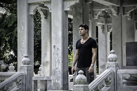 Young man standing on porch of stone temple in Bangkok enjoying surroundings while traveling.の写真素材