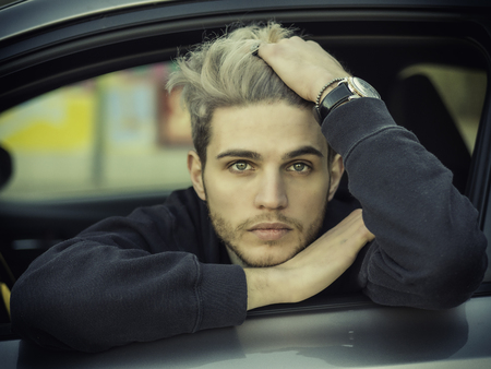 Handsome Blond Young Man Driving a Car, Wearing Black Sweater. hand on wheelの写真素材
