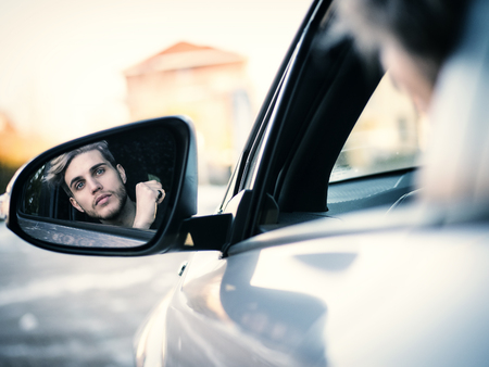 Handsome Blond Young Man Driving a Car, Seen in the Rear Mirrorの写真素材